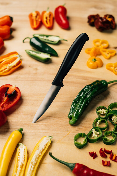 Aufgeschnittene Chilis in Rot, Gelb, Orange und Grün mit einem Messer auf einem Holzbrett